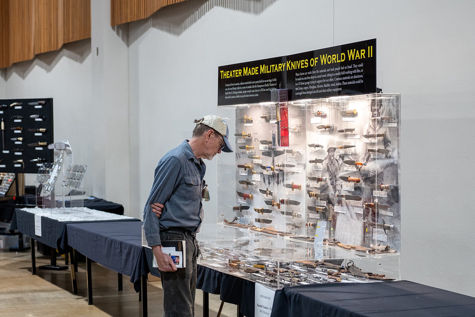 A visitor studies a lit display case of theater-made military knives of World War II