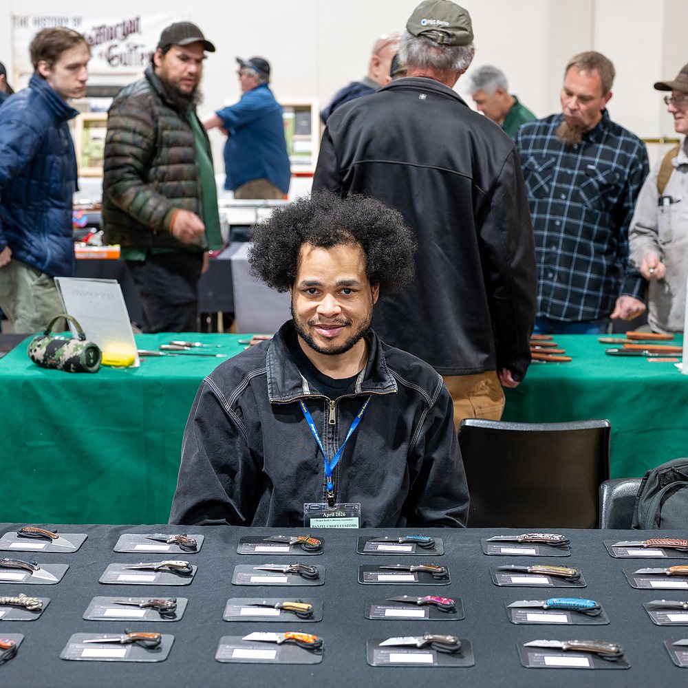 An exhibitor smiles from behind his table of knives