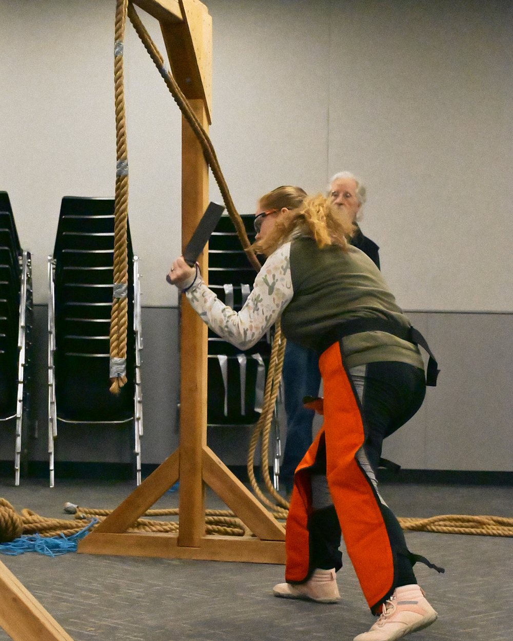 A competitor in safety glasses and protective chaps swings at the rope