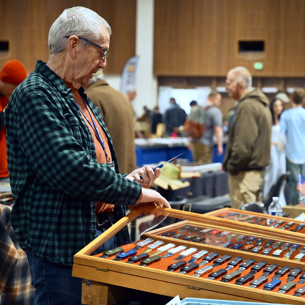 A visitor looks over a dealer's cases of pocket knives at the 2026 show