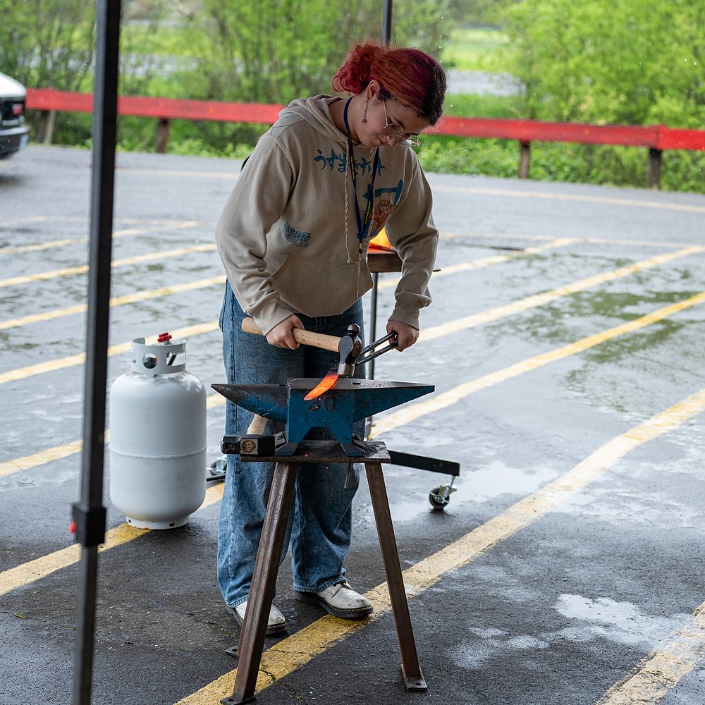 A young smith forges at an anvil at the outdoor demonstration